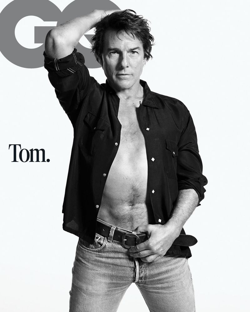 Tom Cruise in an unbuttoned black shirt and denim jeans against a white background for GQ Magazine