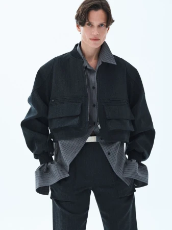 Model wearing a dark utility bomber jacket and striped shirt against a plain white studio background