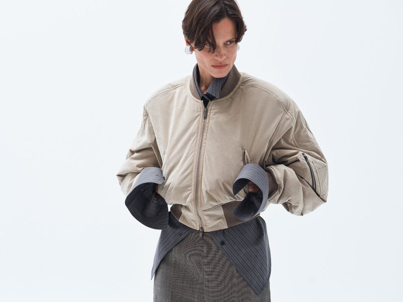 Model wearing a beige bomber jacket over a striped shirt against a plain white background