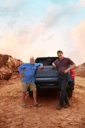 Two men standing next to a blue BYD pickup truck in an outdoor rocky landscape at dusk.