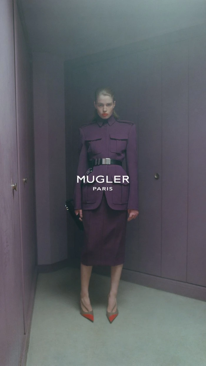 Model standing in a structured plum suit with a belt inside a room with fitted purple wardrobes.