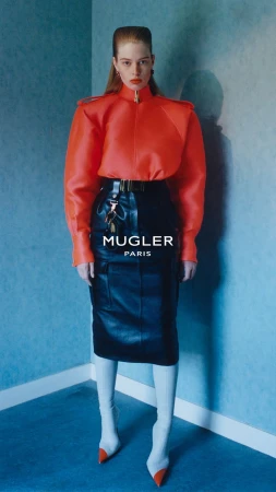 Model in vibrant red structured jacket and black leather skirt standing against a textured blue wall.