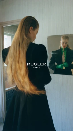 Model with long blonde hair in black apparel looking into a mirror for the Mugler F/W 26 campaign.