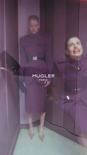 Model in a purple structured belted suit standing inside a mirrored corner interior with Mugler Paris branding