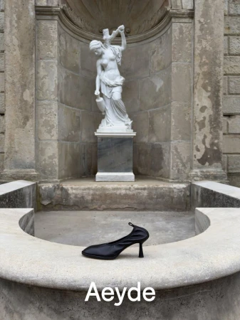 Black heeled shoe resting on a stone fountain ledge with a classical white statue in the background for Aeyde Pre Fall 26