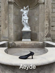 Black heeled shoe resting on a stone fountain ledge with a classical white statue in the background for Aeyde Pre Fall 26
