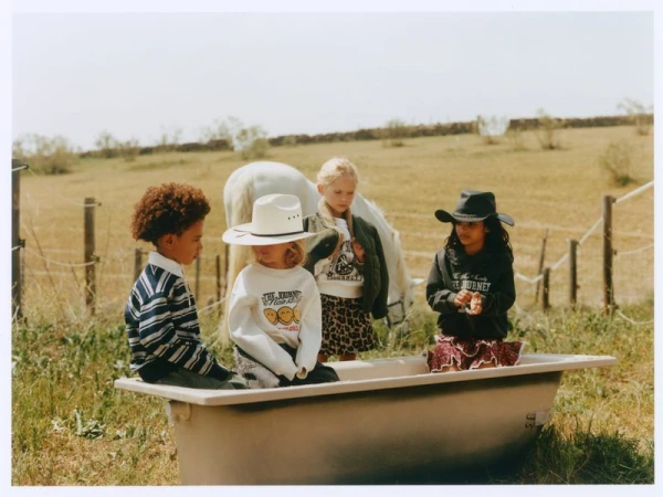 Four children in casual clothing posed together around a vintage bathtub in an open field with a white horse standing behind them.