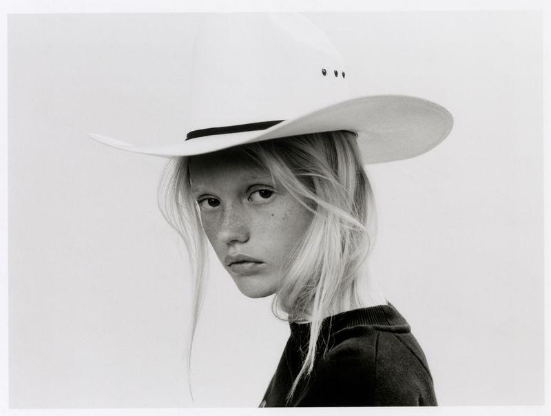 Model with long blonde hair and freckles wearing a white cowboy hat against a light background for The Journey project.