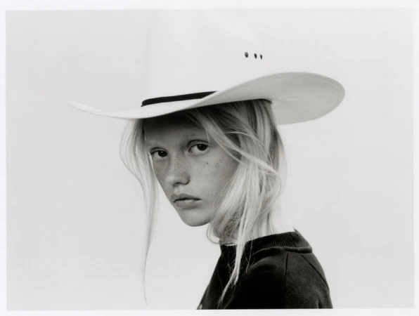 Model with long blonde hair and freckles wearing a white cowboy hat against a light background for The Journey project.