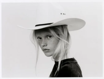 Model with long blonde hair and freckles wearing a white cowboy hat against a light background for The Journey project.