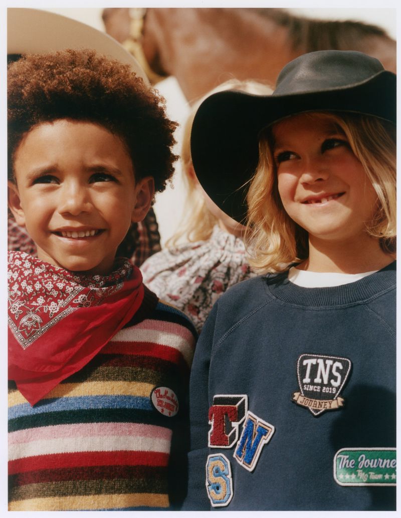 Two smiling children in casual clothing and hats outdoors, photographed by Guille Sanchez for The Journey project.