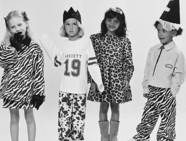 Four children posing together in animal-print and graphic clothing against a plain white studio background.