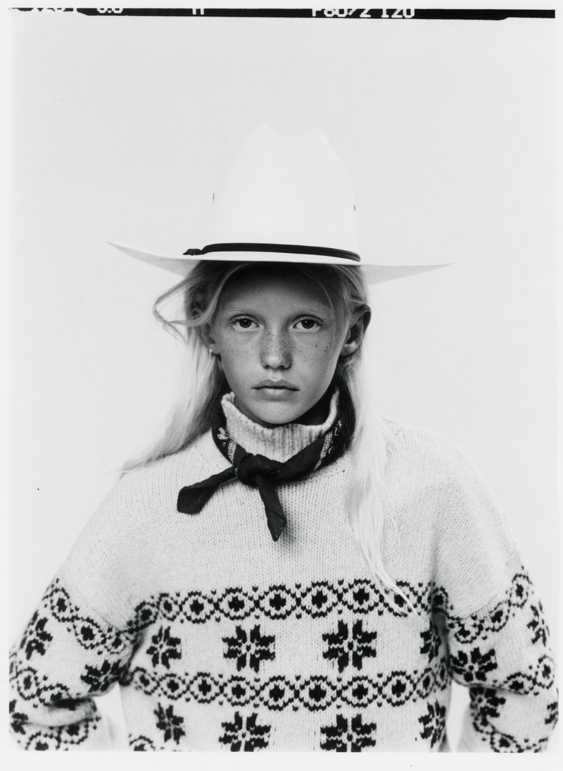 Young model wearing a white cowboy hat and patterned knit sweater against a plain background in a monochrome portrait.