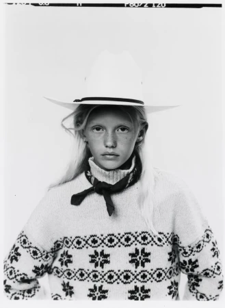 Young model wearing a white cowboy hat and patterned knit sweater against a plain background in a monochrome portrait.