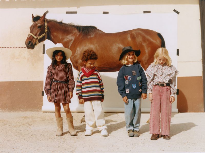 Four children in western-inspired clothing posing in front of a white backdrop with a brown horse.