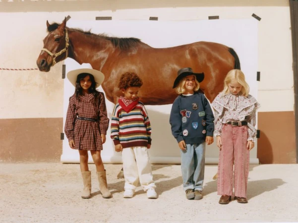 Four children in western-inspired clothing posing in front of a white backdrop with a brown horse.