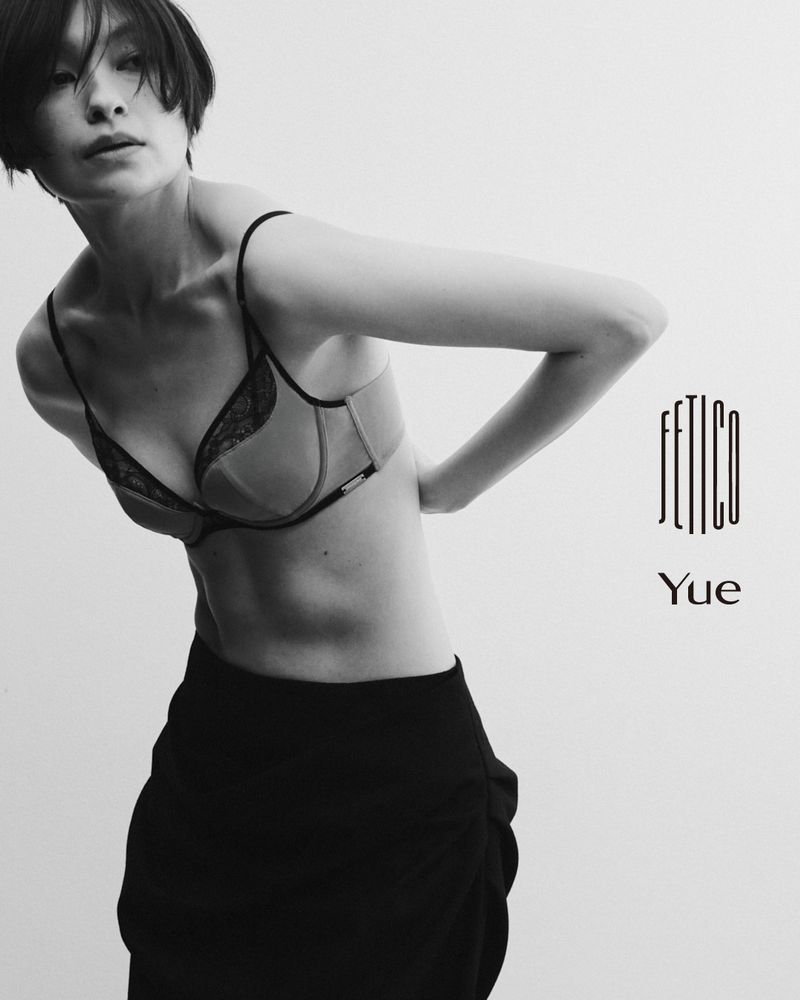 Black and white portrait of a woman wearing a bra and dark skirt against a plain background