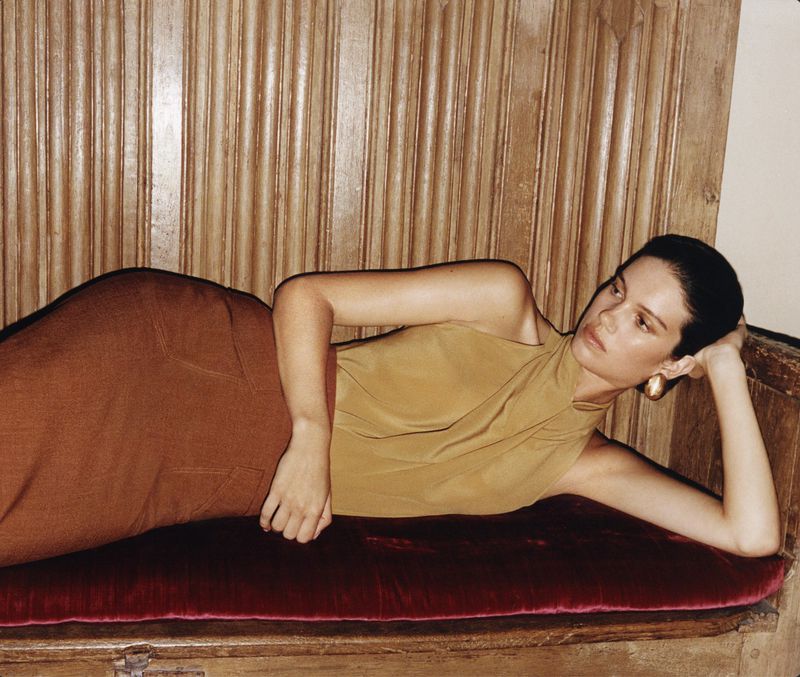 A model reclining on an ornate wooden bench against wood paneling for the Atese F W 2026 campaign.