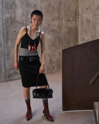 Model with short hair wearing a black dress and holding a handbag in a concrete interior setting