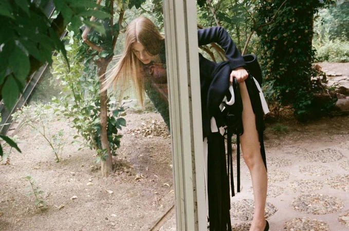Model Anne Floor Wetemans leaning against a glass frame in a greenhouse setting for Harper's Bazaar Italia