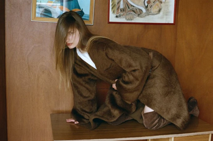 Model Anne Floor Wetemans in a brown coat posing on a wooden surface for Harper's Bazaar Italia