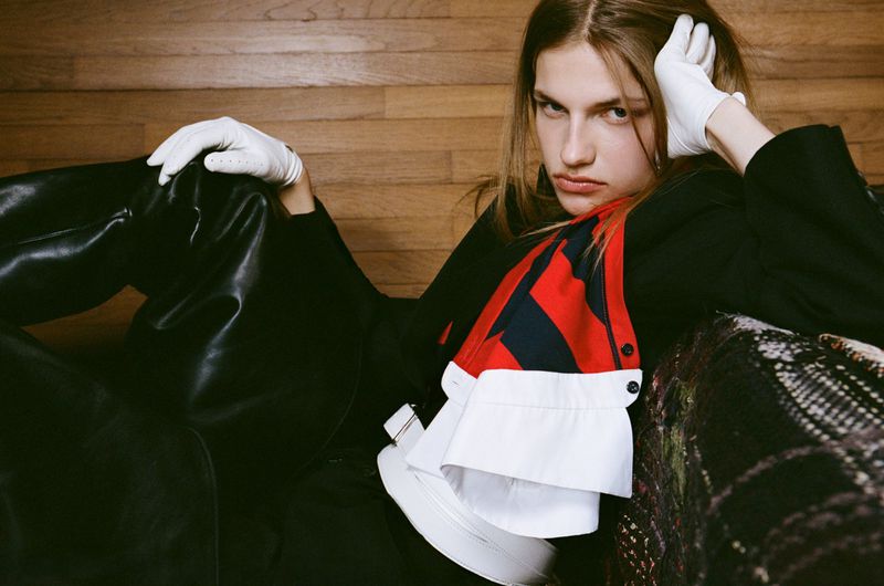 Model Anne Floor Wetemans wearing white gloves and black leather boots against a wood-paneled wall for Harper's Bazaar Italia