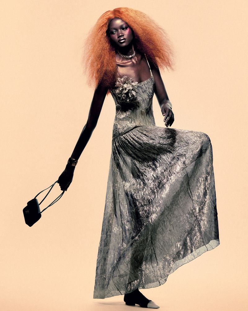 Model Caren Jepkemei with voluminous red hair wearing a grey patterned gown and holding a handbag for AURUM.