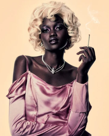 Black woman with blonde curly hair wearing a pink satin top and holding a lit cigarette against a neutral backdrop