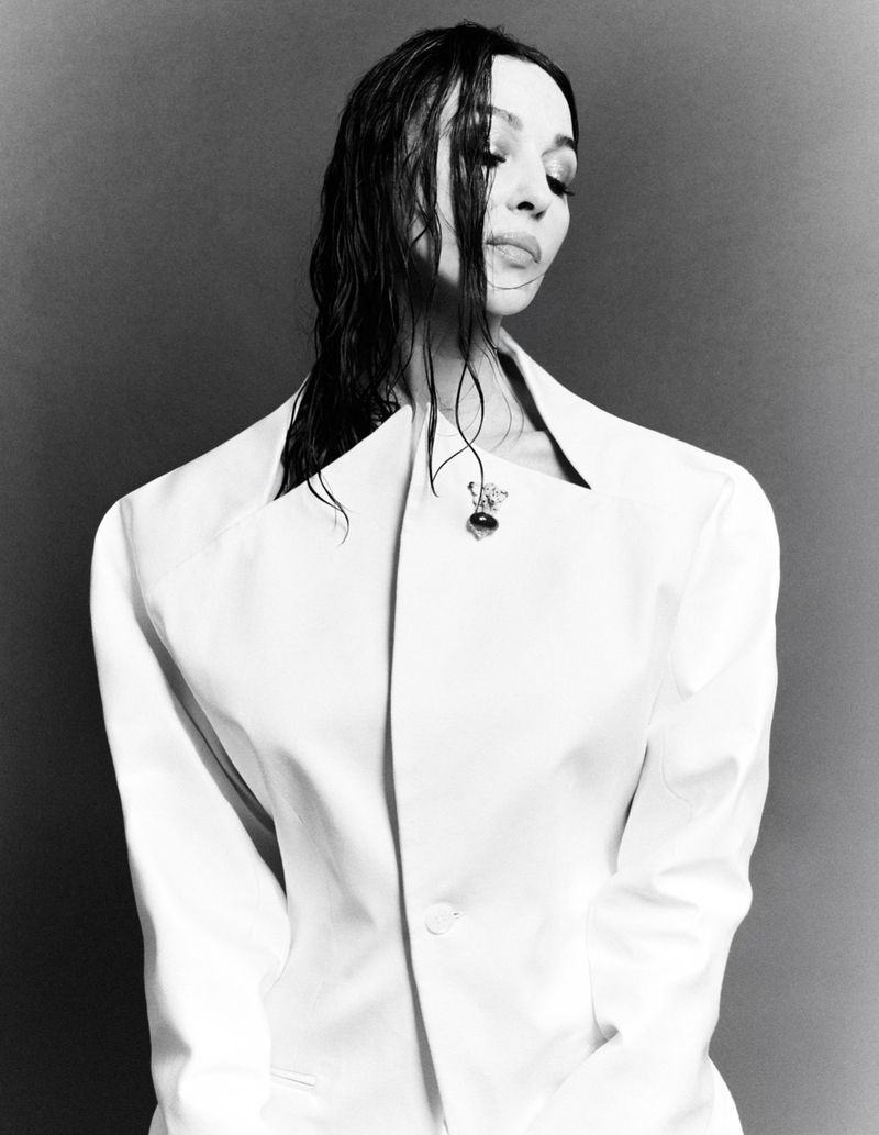 Monochrome portrait of Monica Bellucci wearing a structured white jacket with wet dark hair against a neutral backdrop.