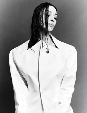 Monochrome portrait of Monica Bellucci wearing a structured white jacket with wet dark hair against a neutral backdrop.