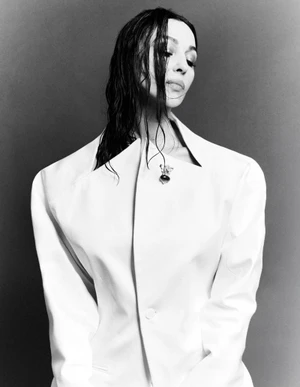 Monochrome portrait of Monica Bellucci wearing a structured white jacket with wet dark hair against a neutral backdrop.