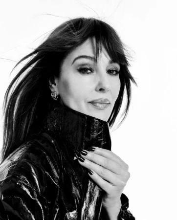 Portrait of Monica Bellucci wearing a dark glossy coat against a white background