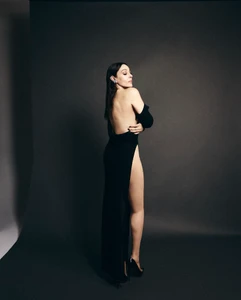 Monica Bellucci posing in a backless black evening gown against a dark grey seamless studio backdrop