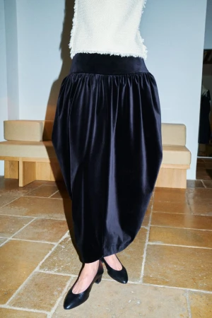 Model wearing a white textured top and voluminous black skirt with black flats in an interior setting