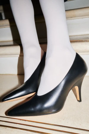 Close-up of feet wearing black leather pointed heels and white tights standing on stairs.