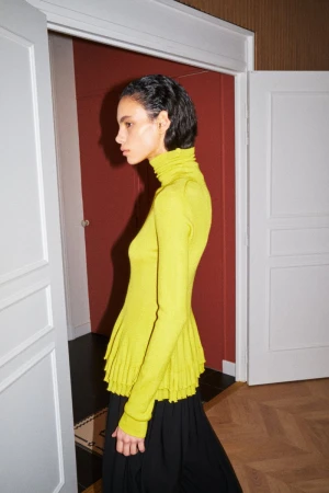 Model in a yellow turtleneck sweater and black skirt standing in a doorway for American Vogue photographed by Ladislav Kyllar.
