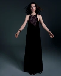 Sylvia Hoeks in a long black halter dress standing against a dark grey seamless studio backdrop.