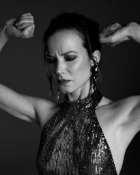 Sylvia Hoeks with eyes closed wearing a sequined halter top and posing against a dark background in a portrait captured by Kourosh Sotoodeh.