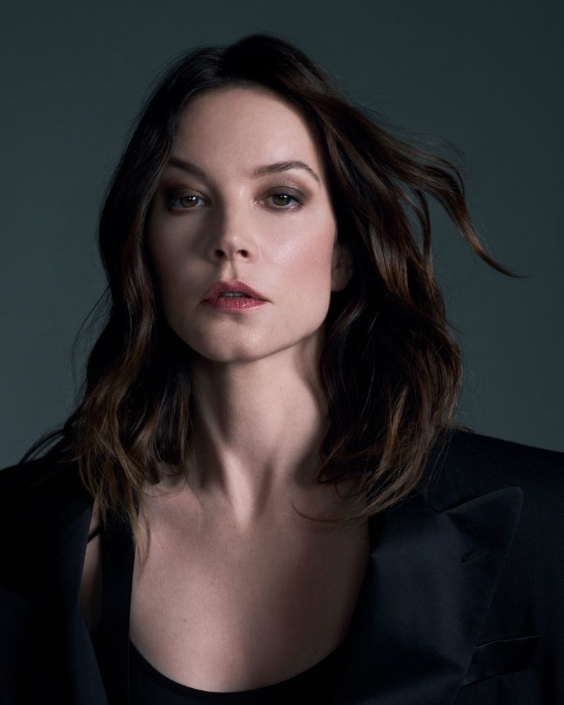 Portrait of actress Sylvia Hoeks with dark hair wearing a black jacket against a dark studio background