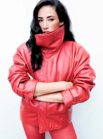 Woman with long dark hair wearing a high-collared red leather jacket against a seamless white background for The Perfect Magazine.