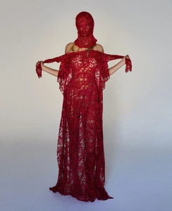 Model wearing a floor-length red lace gown and matching head covering against a neutral studio backdrop.