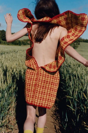 Model running through a grassy meadow wearing a red and yellow patterned backless dress with a ruffled collar.