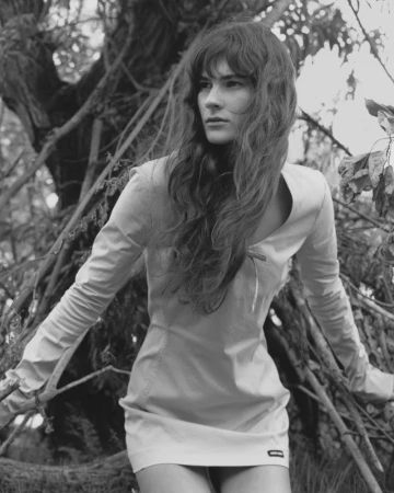 Monochrome fashion portrait of a model with long wavy hair standing among dense woodland branches.