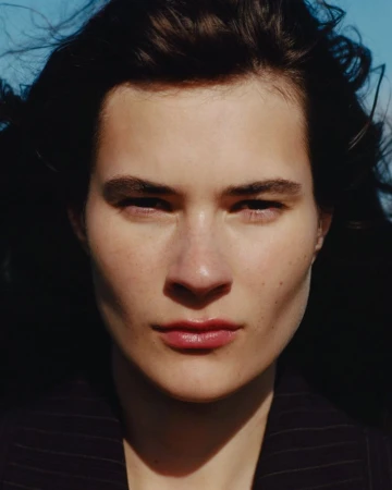 Close-up portrait of a model with dark hair against a bright blue sky for Heroine Magazine