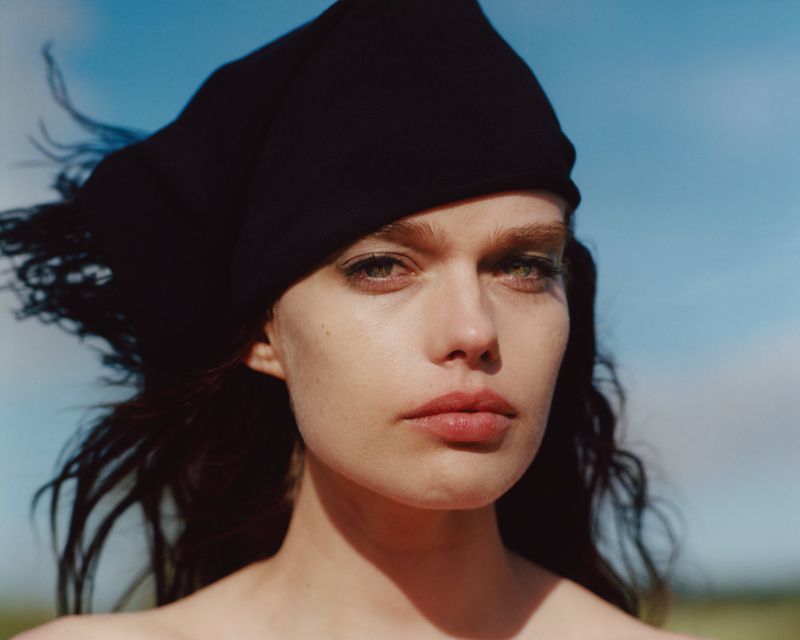 Close-up portrait of a woman wearing a black headscarf against a clear blue sky background.