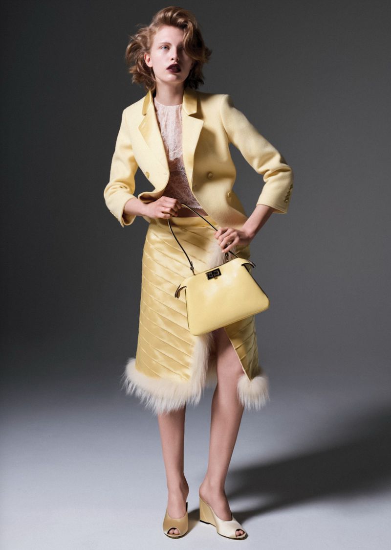 Woman in a yellow skirt suit holding a handbag in a studio setting, fashion photography.