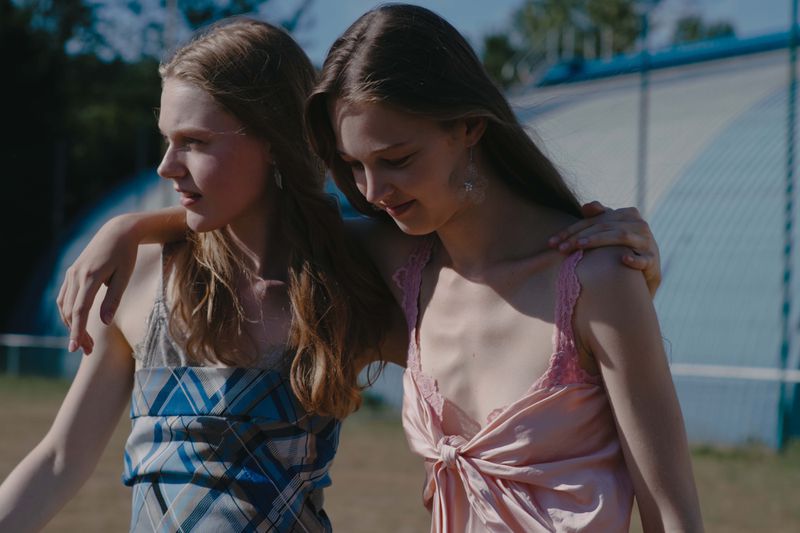 Two young female models walking arm in arm outdoors wearing patterned dresses against a blurred background