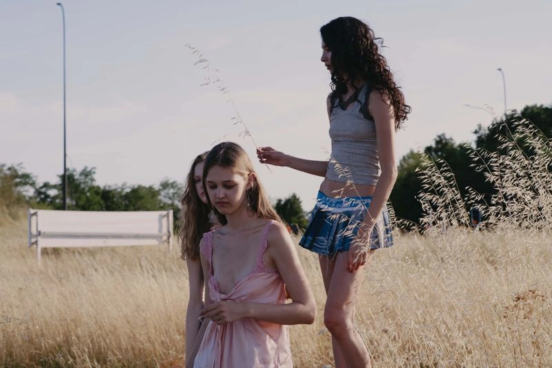 Three models in a tall dry grassy field during daylight, captured by photographer Arianna Genghini.