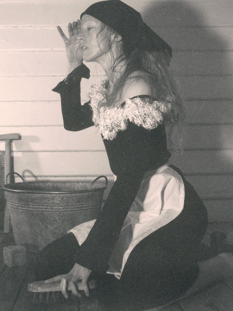 Model Raquel Zimmermann in a black top with white ruffles kneeling next to a wash tub for W Magazine, photographed by David Sims