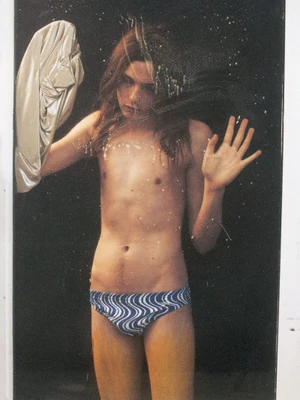 Model standing behind a glass surface holding a metallic silver fabric with one hand and touching the glass with the other.